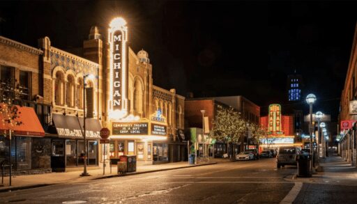 Night outdoor photo of the Michigan and State Theaters, long shot off Liberty St with the marquees lit and full buildings in view